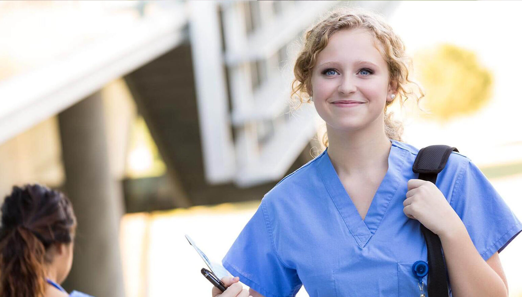 A young nurse in scrubs walks with a backpack