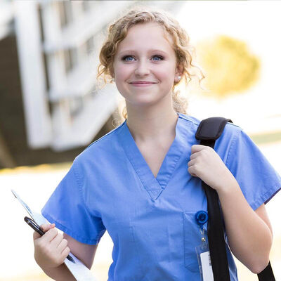 A young nurse in scrubs walks with a backpack