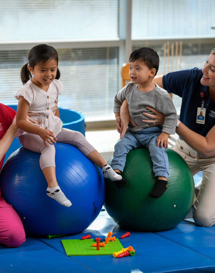 Image of faculty member smiling and helping two pediatric patients with a student.