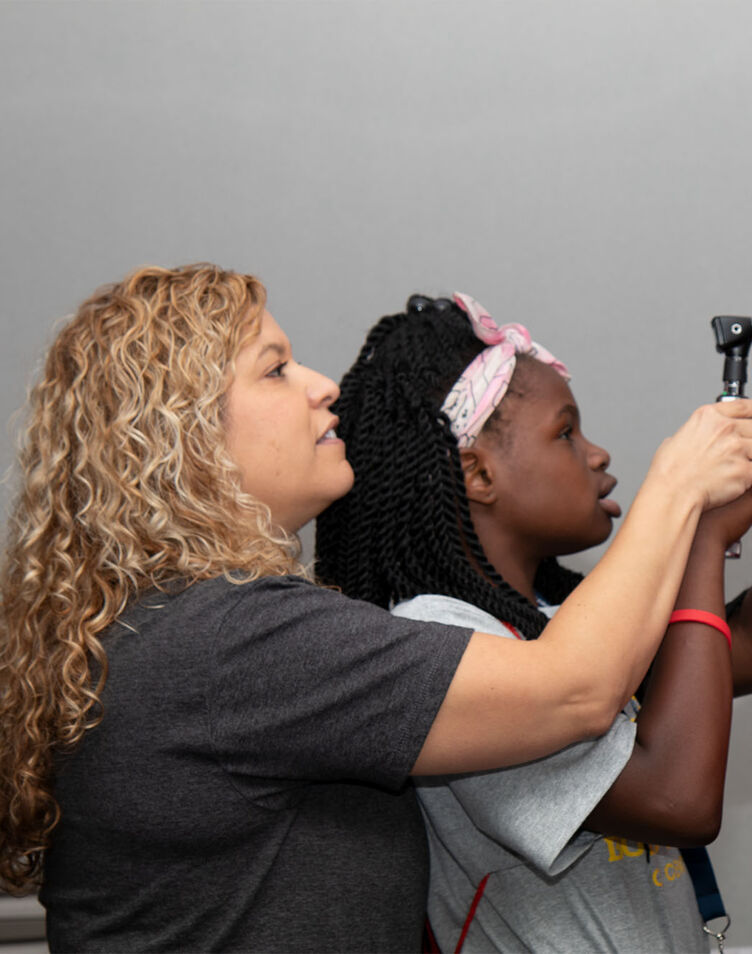 A female nursing student demonstrating an eye exam to two young children
