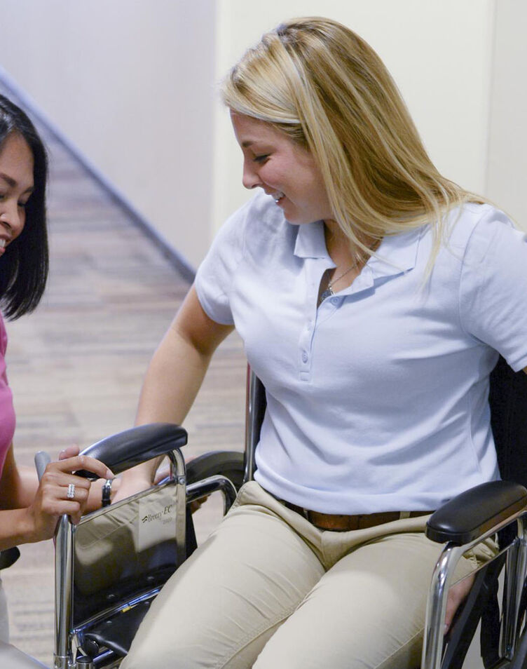 Two female occupational therapy students practicing skills in a wheelchair